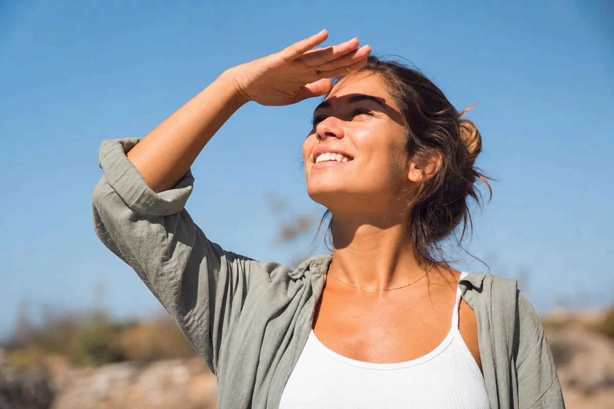 Personne qui sort à l'extérieur en plein soleil, main levée pour se protéger les yeux de la lumière vive
