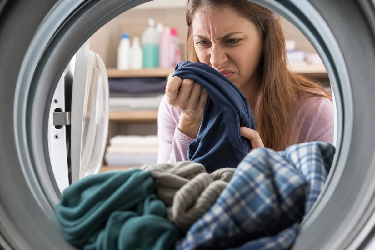 Linge propre plié posé près d'un lave-linge ouvert, intérieur du tambour visible