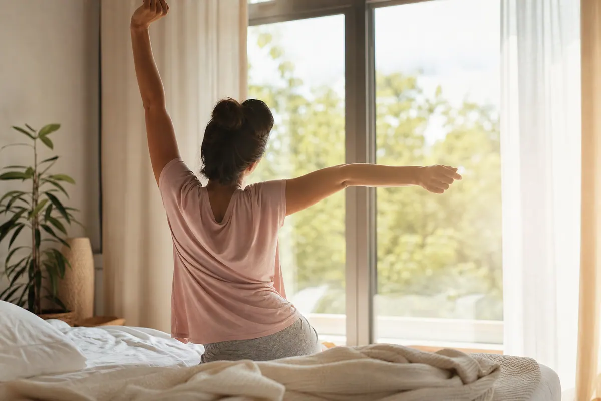 Personne qui s'étire le dos et les bras au réveil, lumière naturelle du matin, ambiance détendue