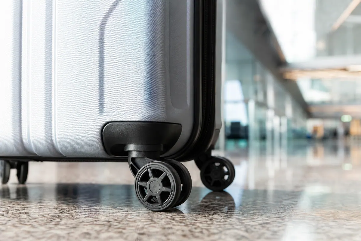 Valise cabine à quatre roulettes posée au sol dans un hall d'aéroport, avec un gros plan sur une roulette